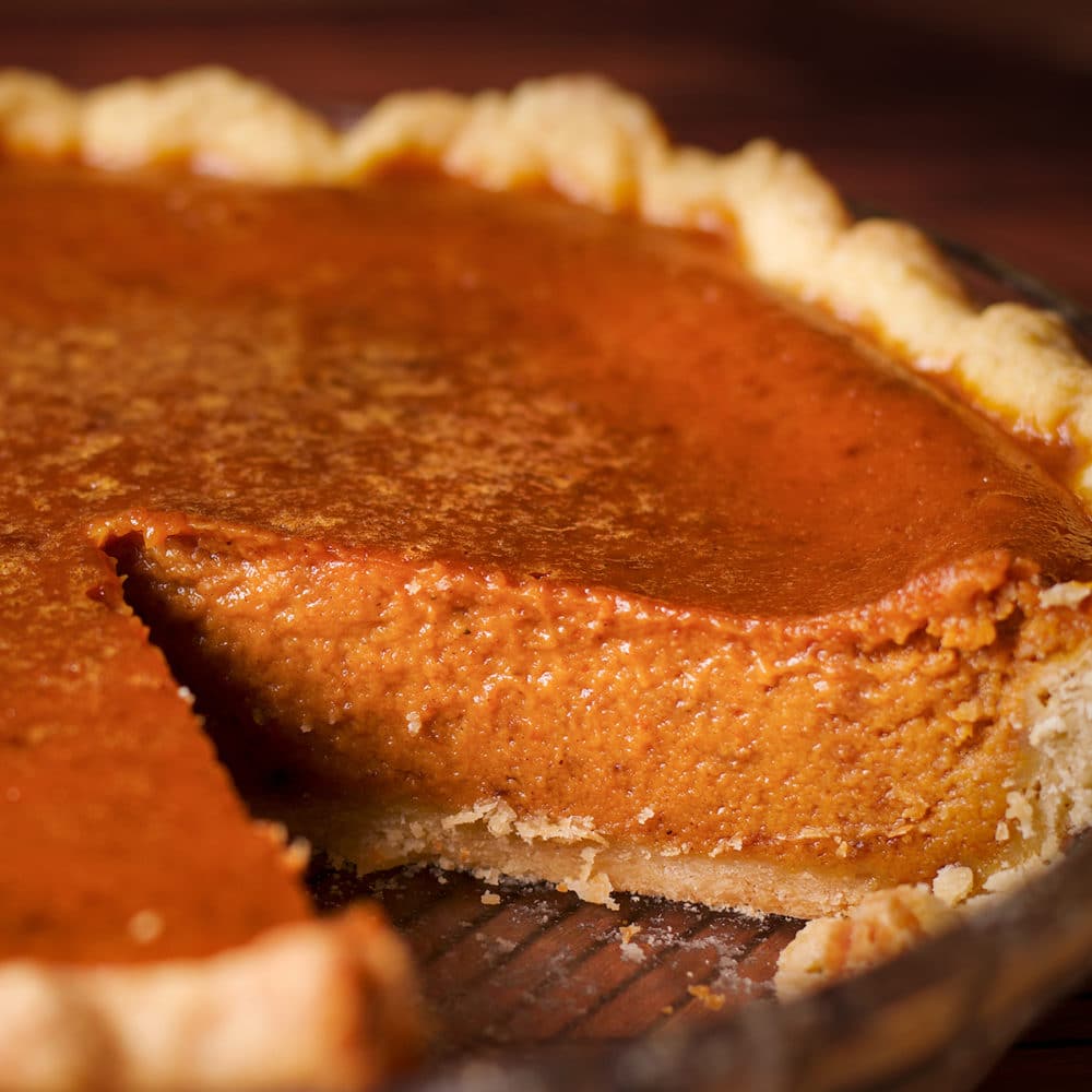 A pumpkin pie with one slice removed so you can see the creamy interior of the filling.