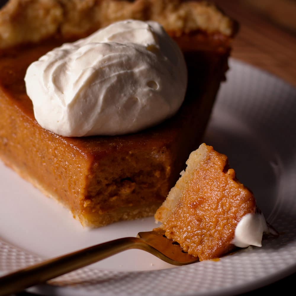 A close up photo of a bite of Maple Pumpkin Pie on a fork that's lying on a white plate.