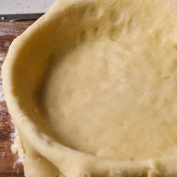 Pie crust dough fitted into a pie plate before the edges are trimmed.