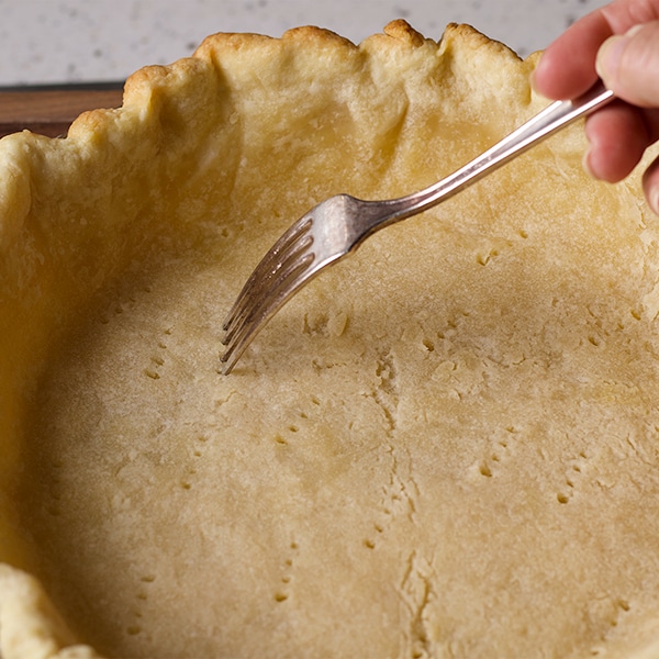 Poking holes in the bottom of a pie crust before baking.