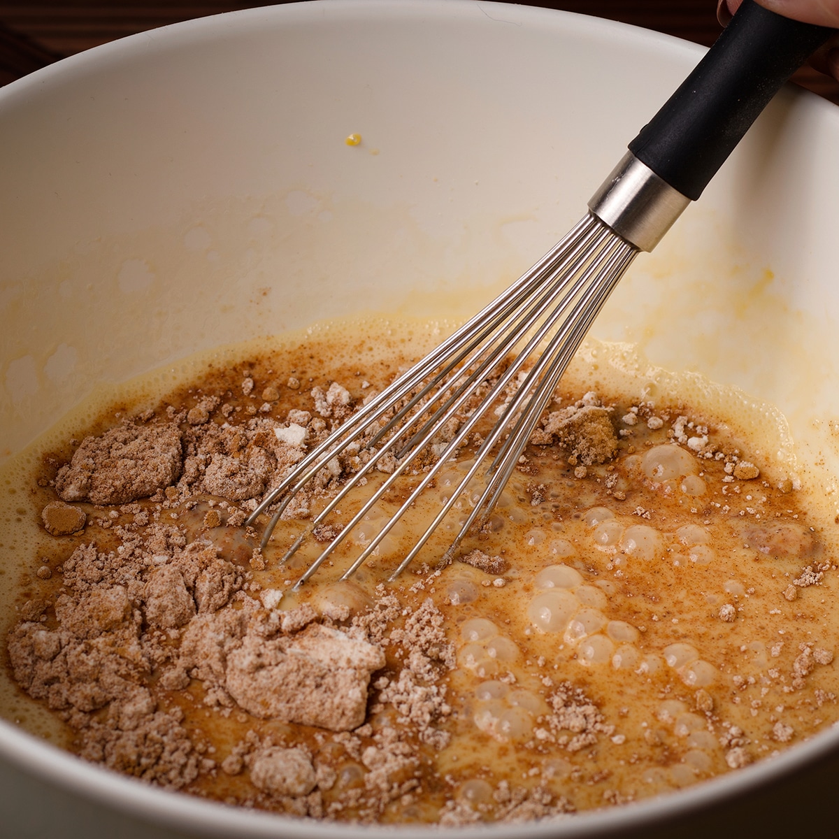 Someone using a wire whisk to blend brown sugar, flour, and pumpkin pie spices into pumpkin pie batter.