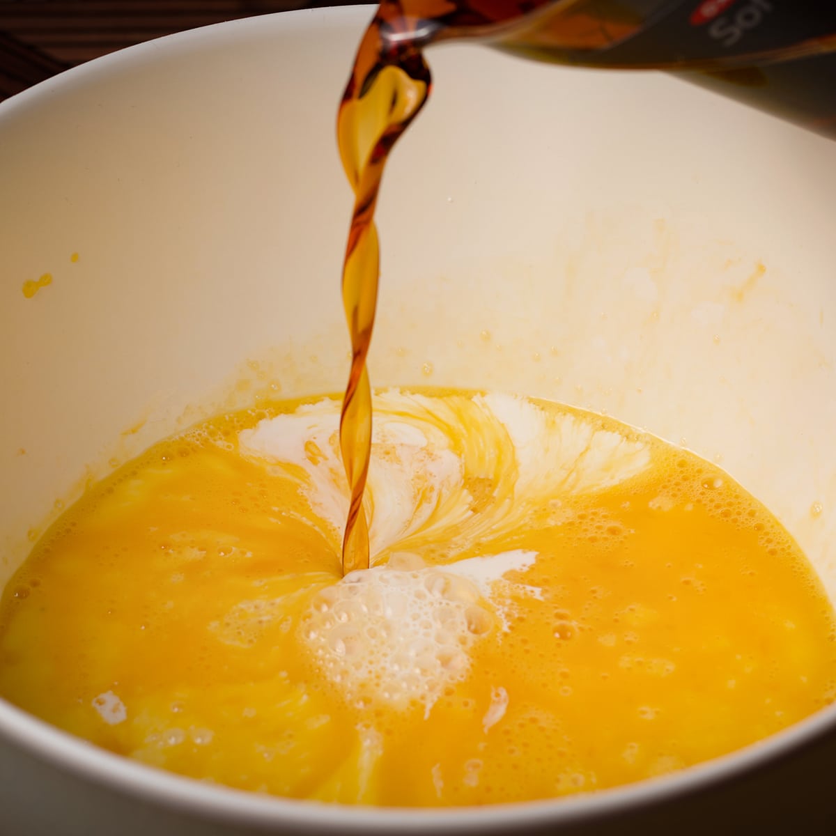 Someone pouring maple syrup and cream into a bowl that contains beaten eggs.