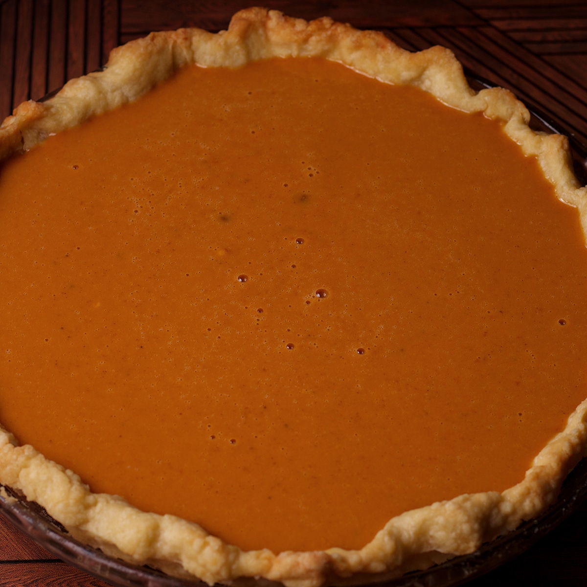 A partially baked pie crust that's been filled with pumpkin pie batter.