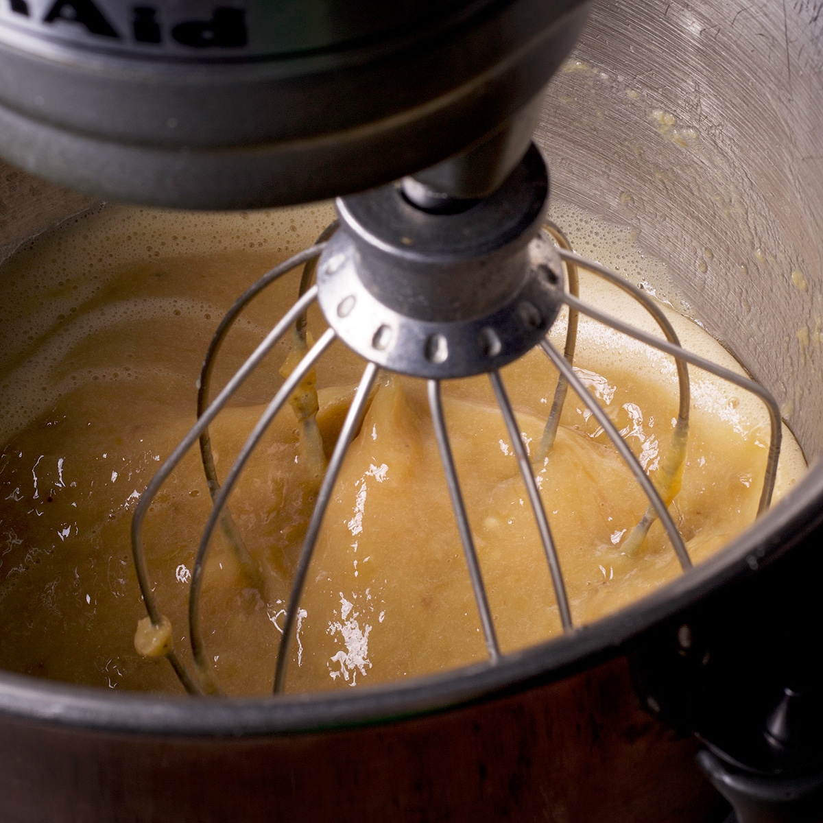 Looking down into the bowl of a stand mixer while it beats the wet ingredients for gluten free banana muffin batter.