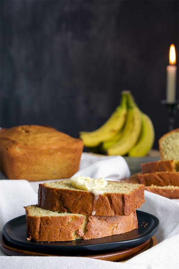 Two pieces of banana bread with butter on a plate. 