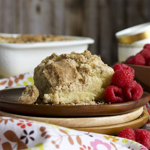 A slice of crumb cake on a plate with raspberries.