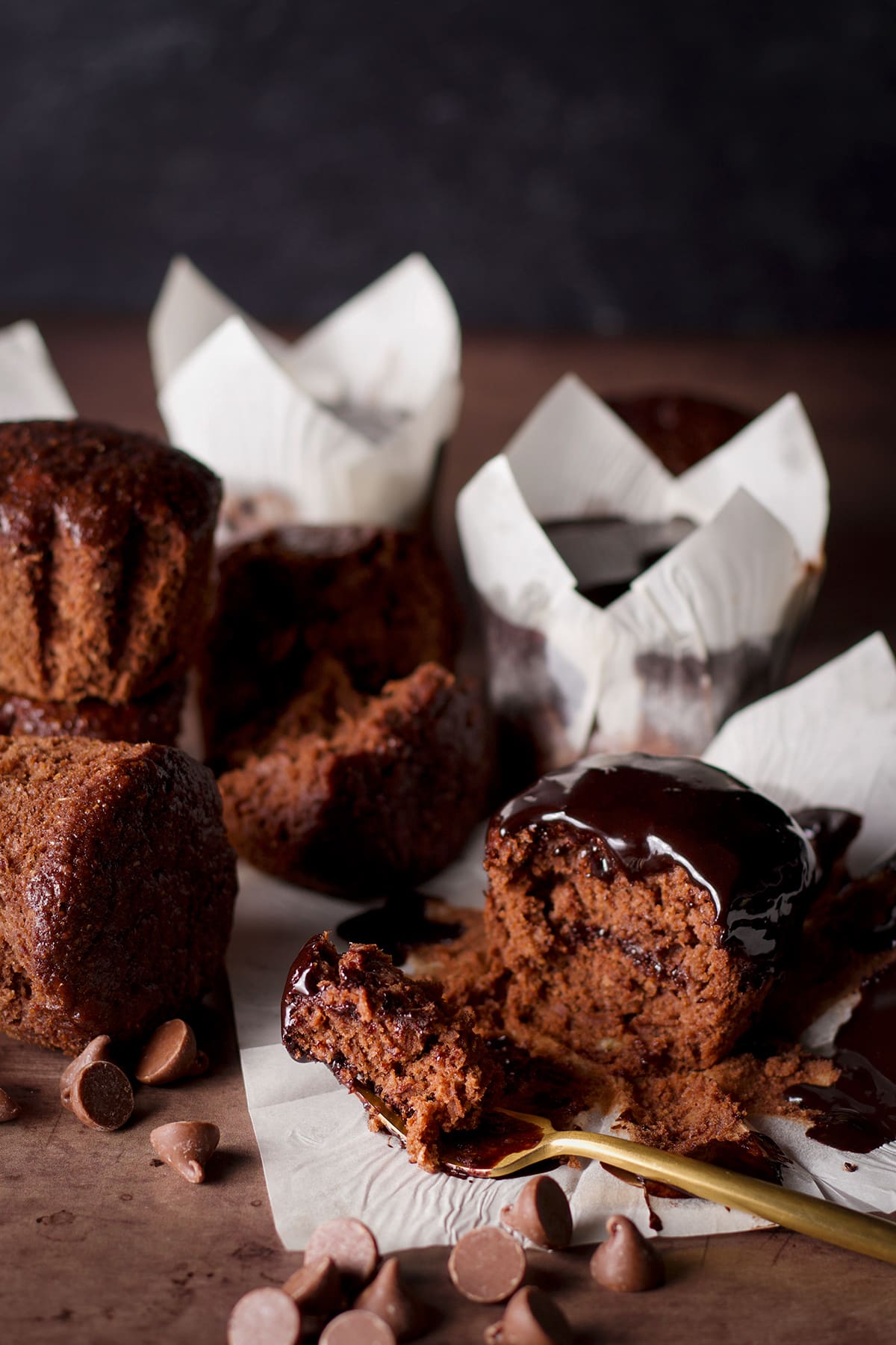 Healthy chocolate banana muffins on a table with chocolate chips scattered around them.