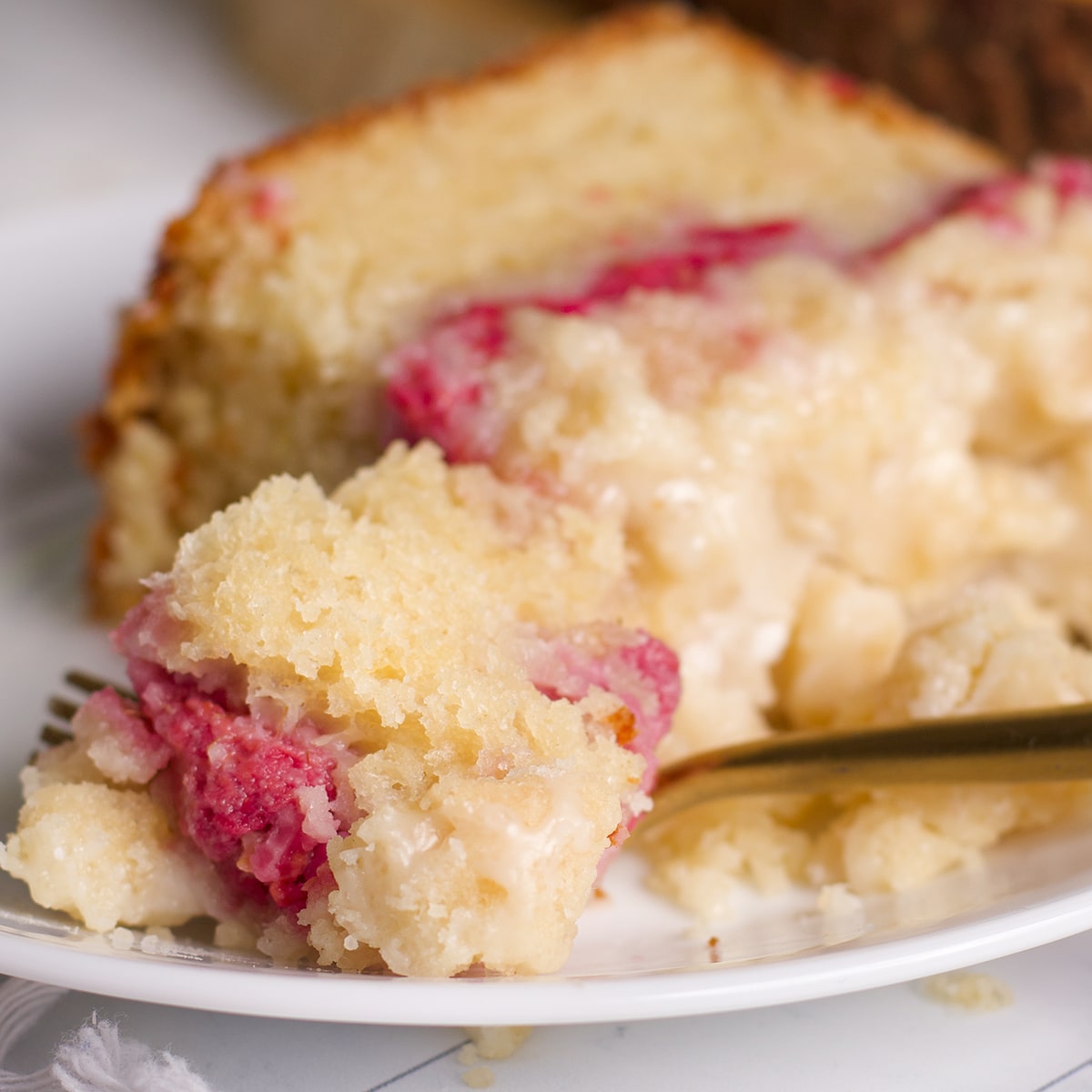 Someone using a fork to cut a bite of raspberry bread from a slice on a white plate.