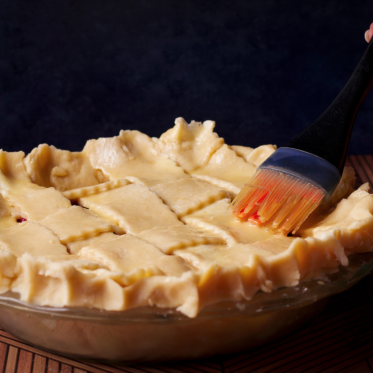 Using a pastry brush to coat the top of a pie crust with egg wash.