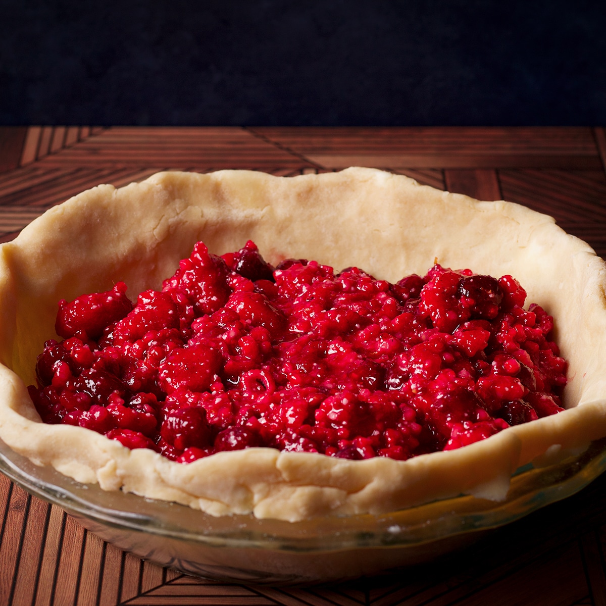 Adding raspberry pie filling to a pie plate that's been lined with pie pastry.