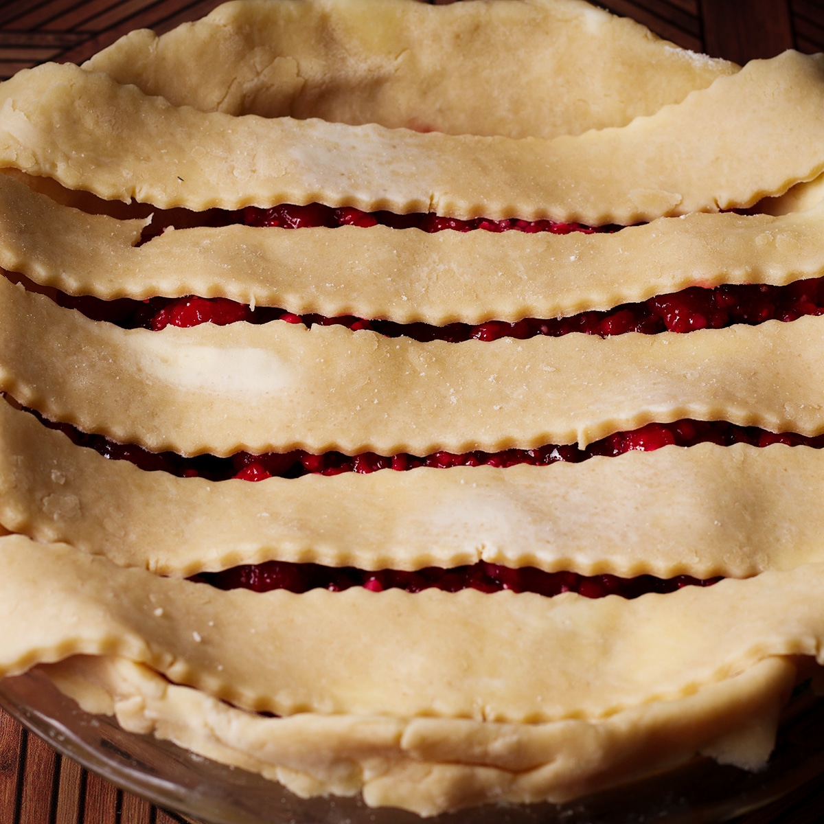 The first step in creating a lattice pie crust is to lay strips of pie dough over the pie, arranging them parallel to each other.