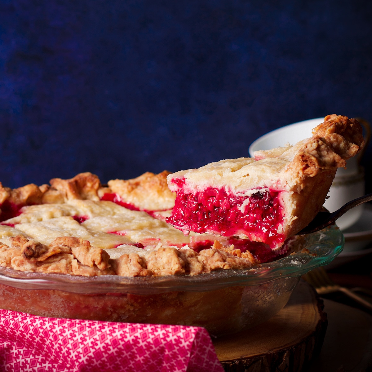 Using a pie server to lift a slice of raspberry pie from the pie plate to serve.