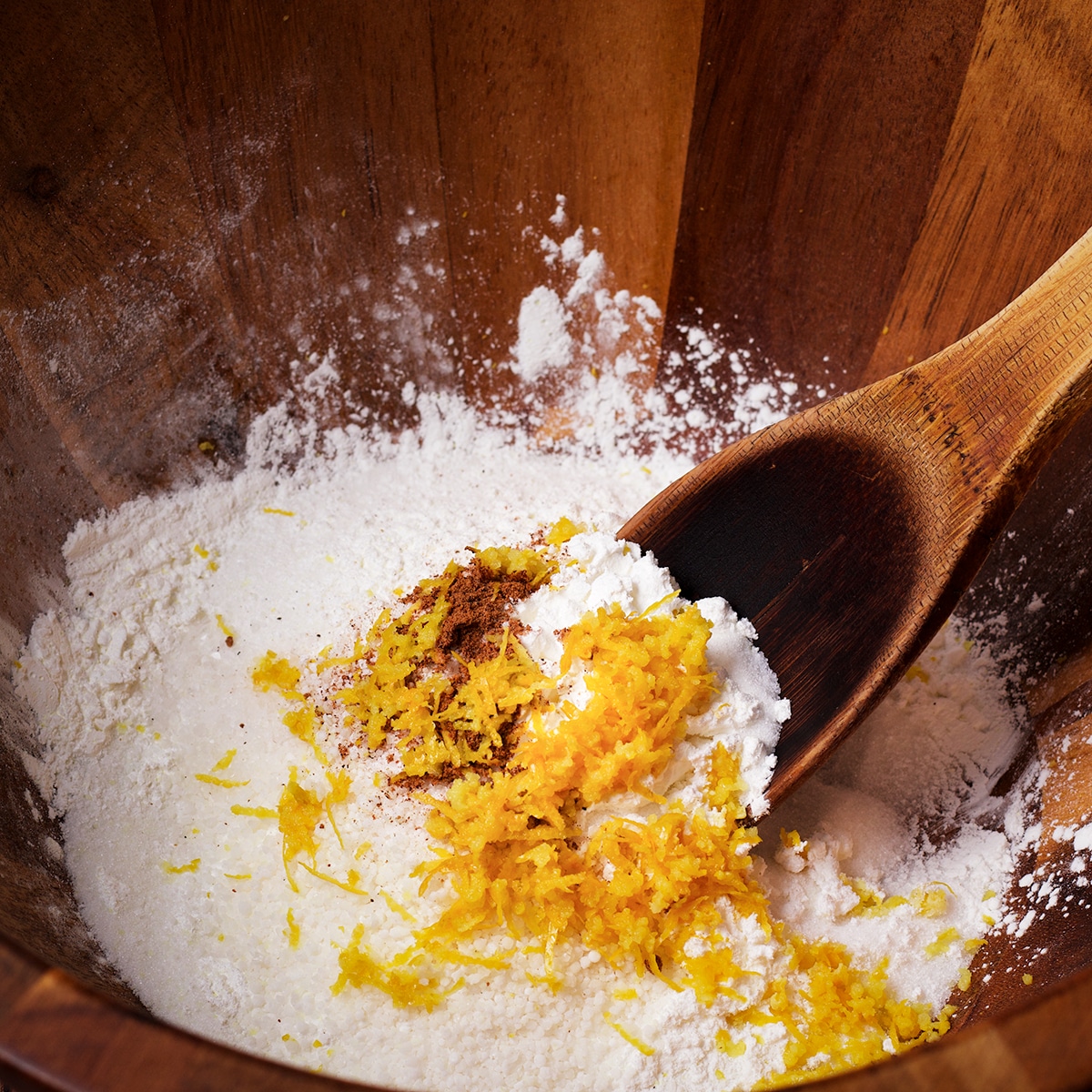Using a wooden spoon to stir sugar, cornstarch, tapioca, nutmeg, and lemon zest.