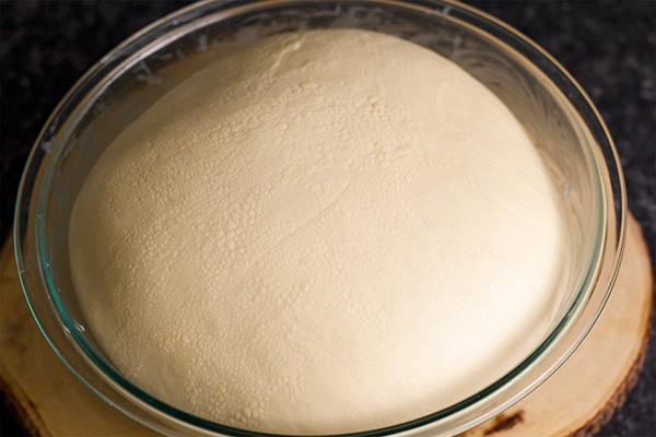 A bowl with bread dough that's risen and ready to be shaped into dinner rolls.