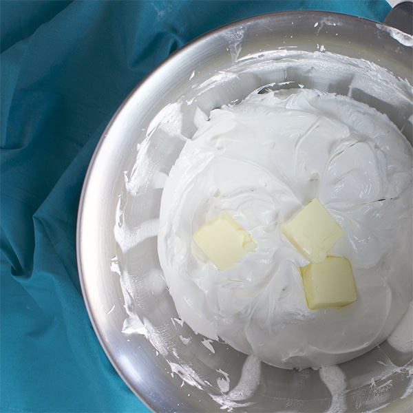 Three pats of butter in a bowl that's filled with Italian meringue.