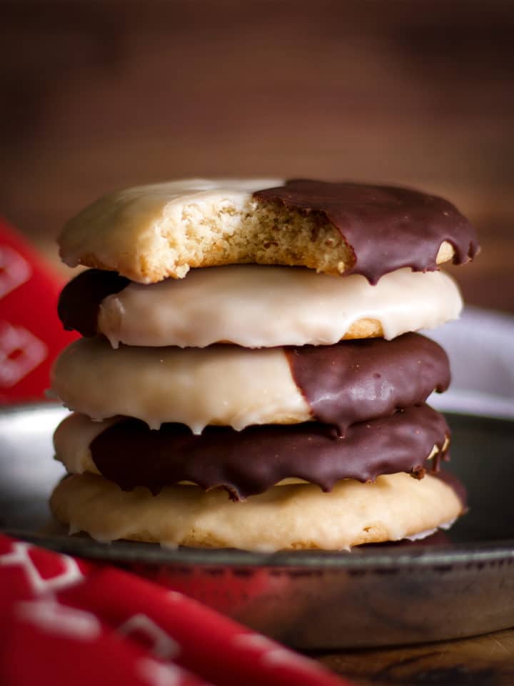 A stack of New York Black and White Cookies, the top cookie has a bite taken out of it.