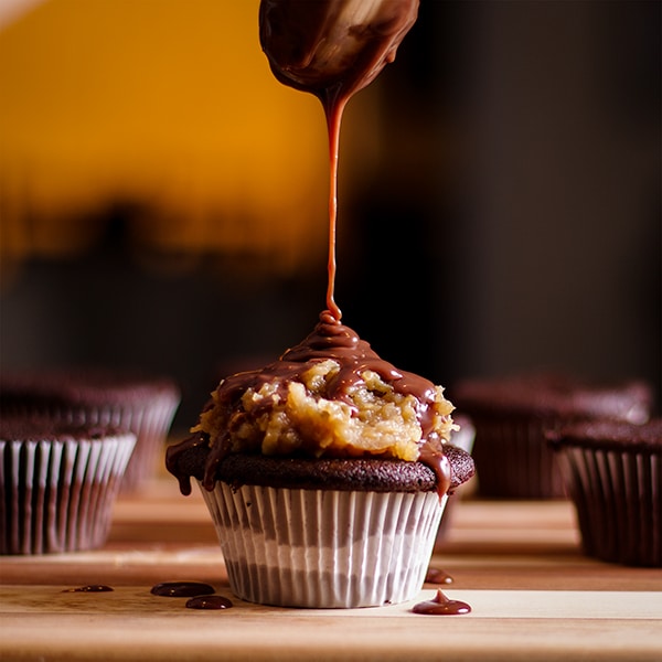 Drizzling chocolate ganache over the top of a German Chocolate Cupcake