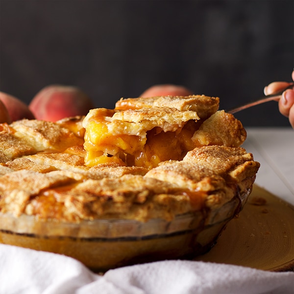 Serving a slice of peach pie with a lattice crust.