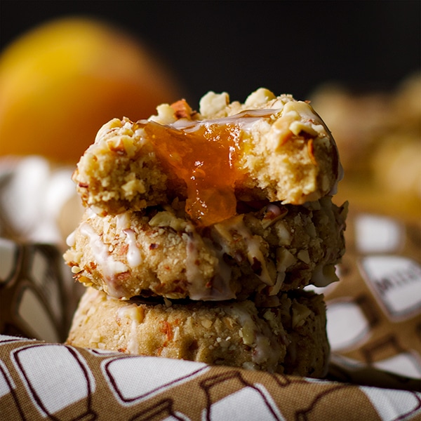A stack of peach almond thumbprint cookies with a bite taken out of one cookie.