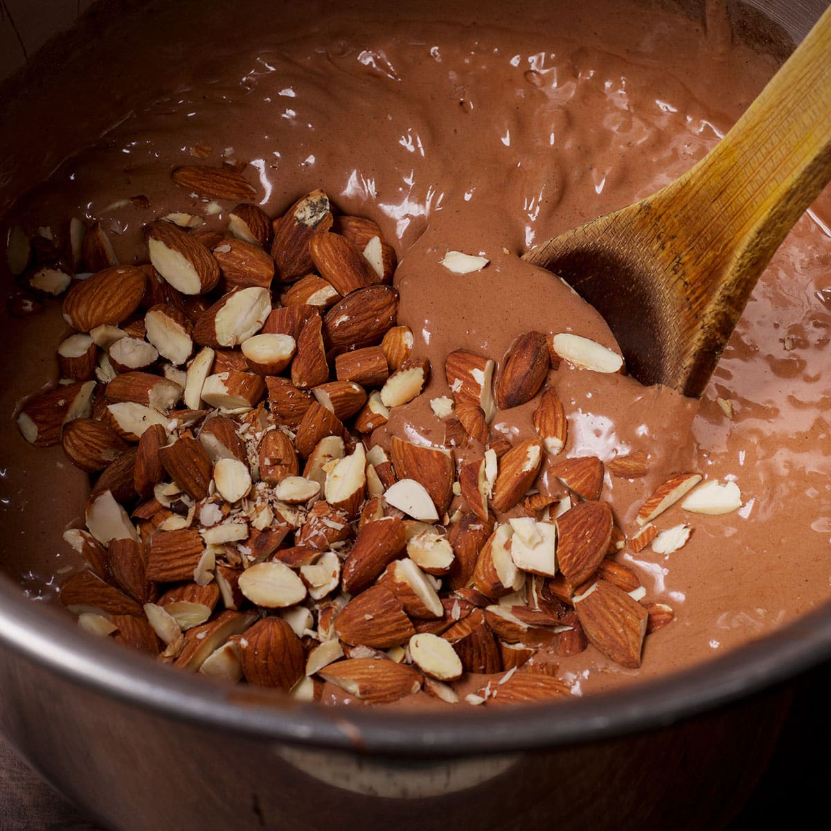 Using a wooden spoon to stir chopped almonds into chocolate pie batter.