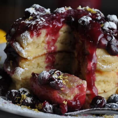 A tall stack of lemon ricotta pancakes covered in blueberry sauce.