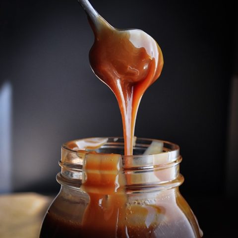 Drizzling salted caramel sauce from a spoon into a jar.