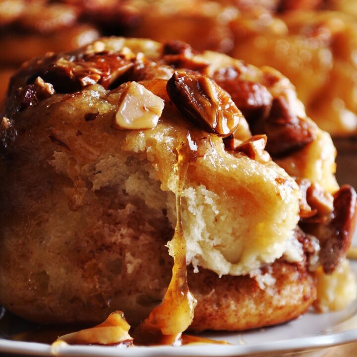 A homemade sticky bun on a plate with caramel dripping down the sides of the roll.
