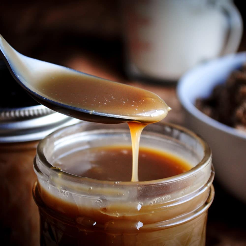 Someone lifting a spoonful of butterscotch sauce from a jar.