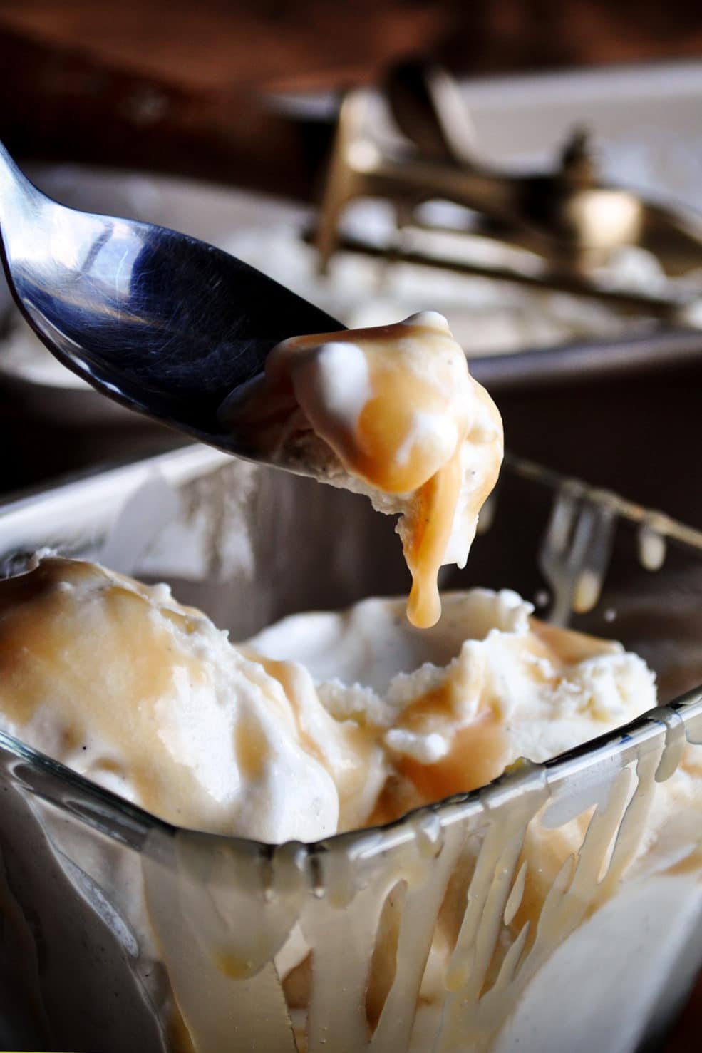 Someone lifting a spoonful of vanilla ice cream from a bowl with butterscotch sauce dripping from the ice cream.