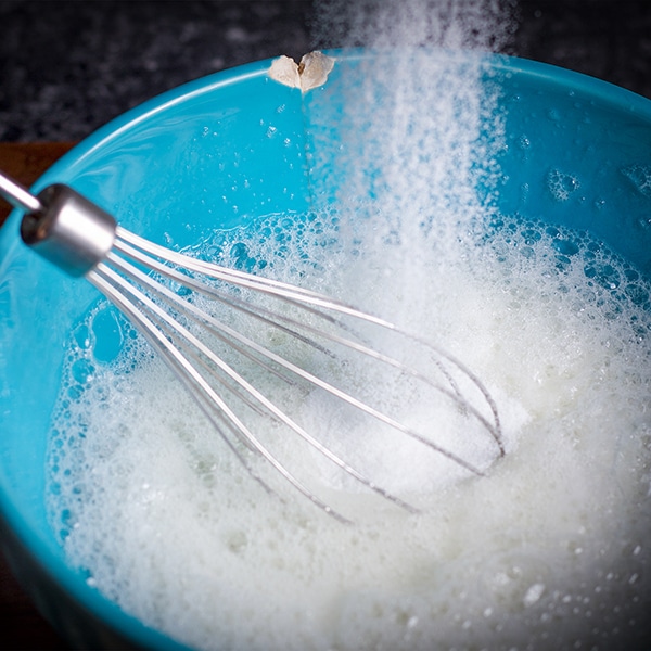 Adding sugar to egg whites while beating them.
