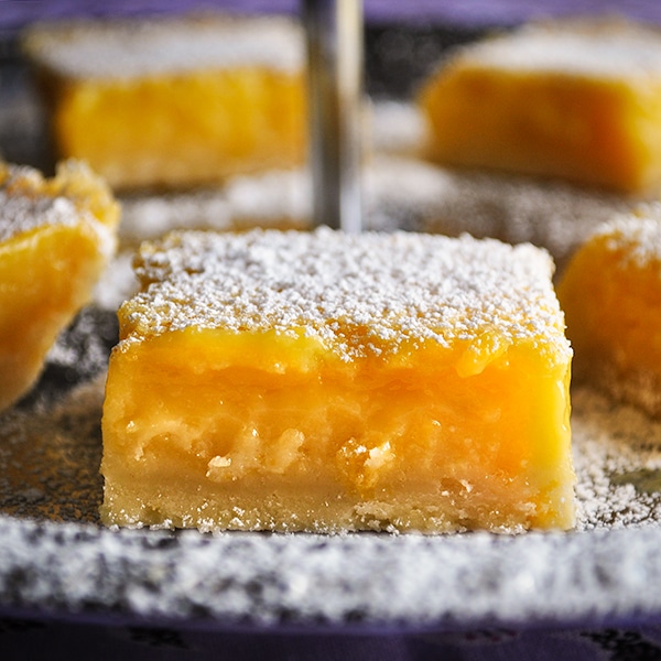 A silver serving platter filled with freshly baked lemon squares dusted with powdered sugar.