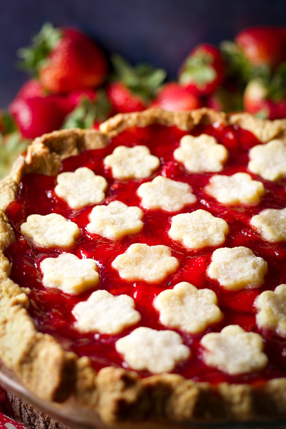 A freshly baked strawberry cream pie cooling on a pie rack with fresh strawberries in the background.