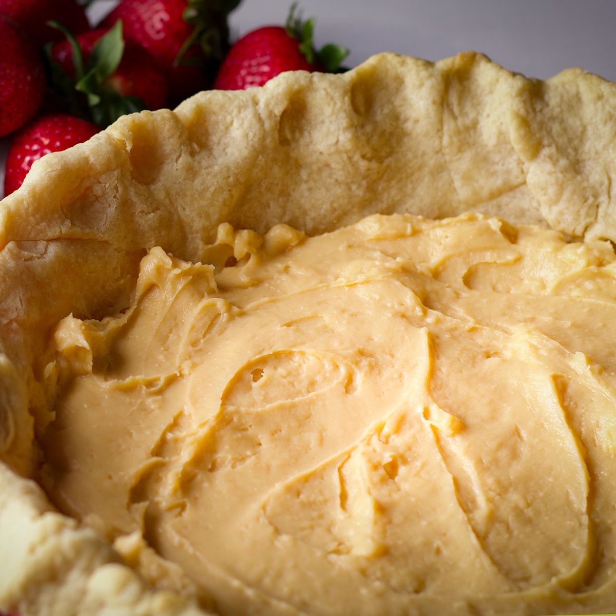 A partially baked pie crust that's been filled with a layer of pastry cream.