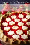 A freshly baked strawberry cream pie cooling on a pie rack with fresh strawberries in the background.