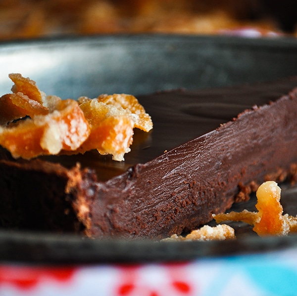 A slice of chocolate orange truffle tart with candied orange peel on a plate.
