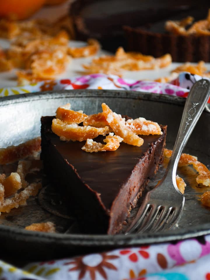 A slice of chocolate orange truffle tart on a plate with a fork.