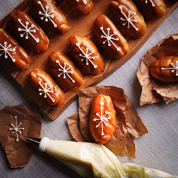 A tray of mini butterscotch eclairs decorated with a white chocolate snowflake design.