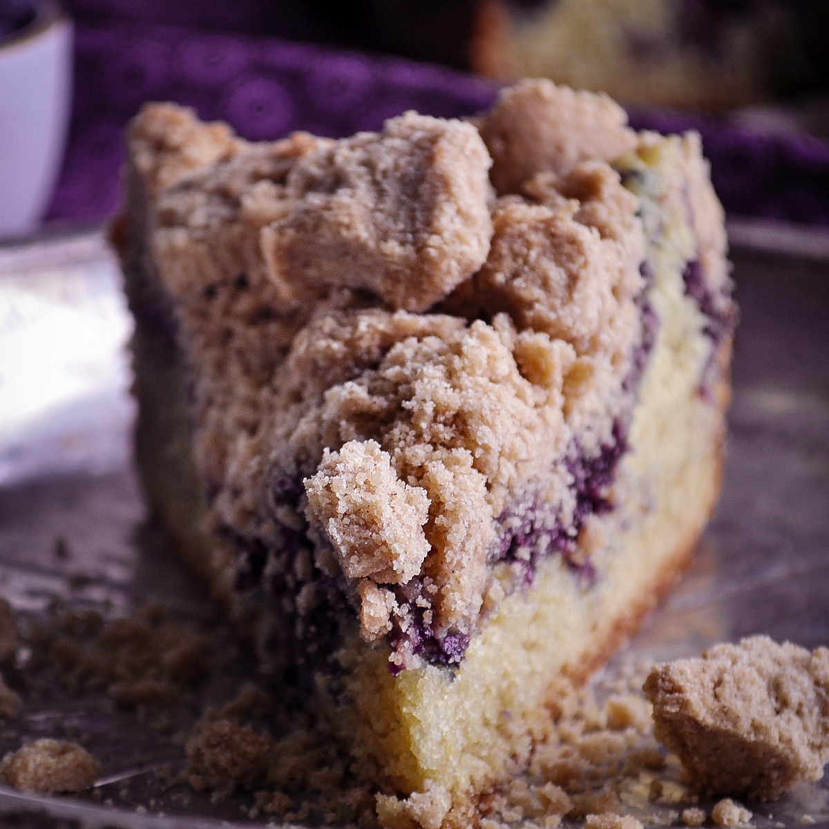 A slice of blueberry crumb cake on a tin plate.