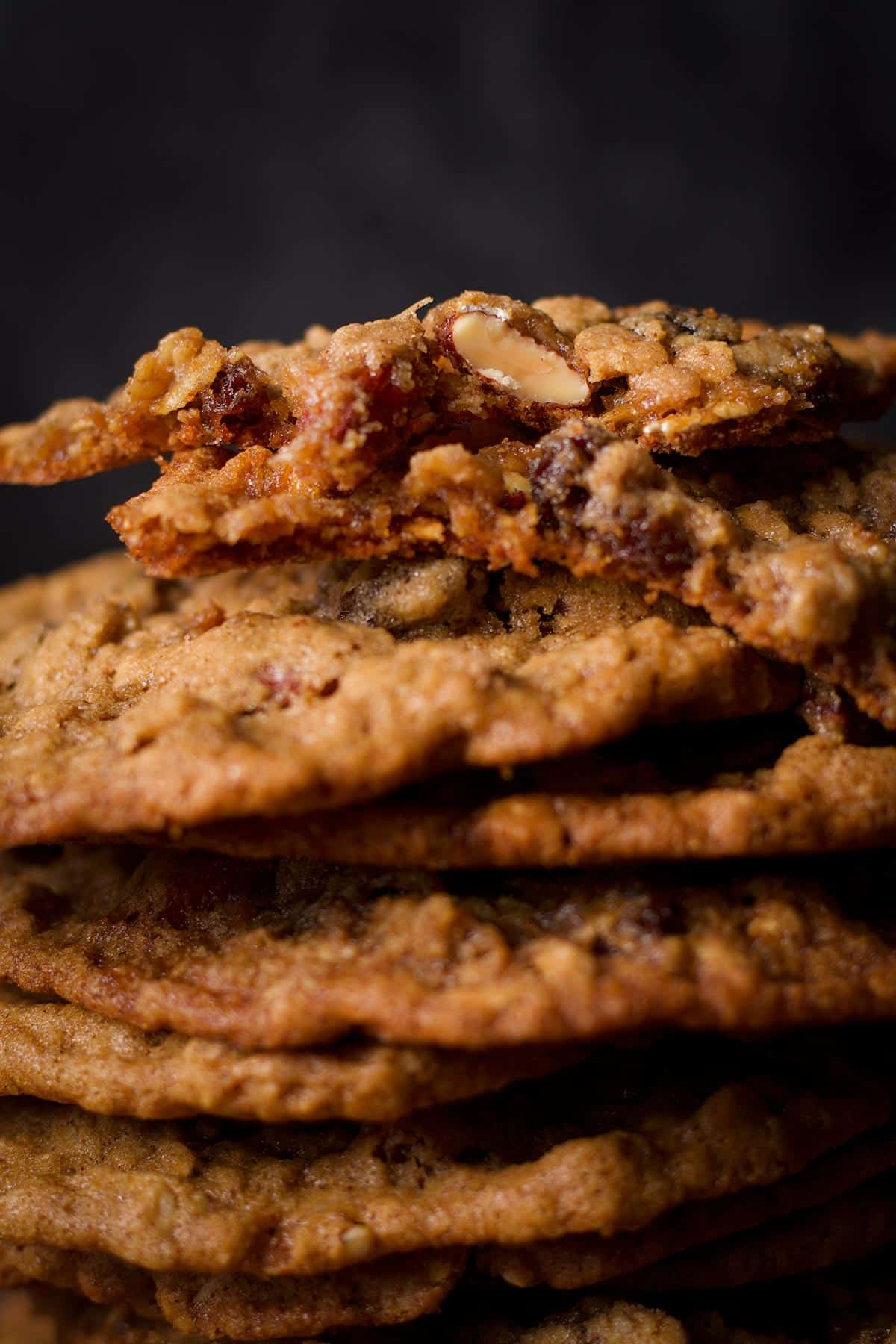 A stack of oatmeal raisin cookies with the top cookie broken in half to reveal the soft, chewy center.