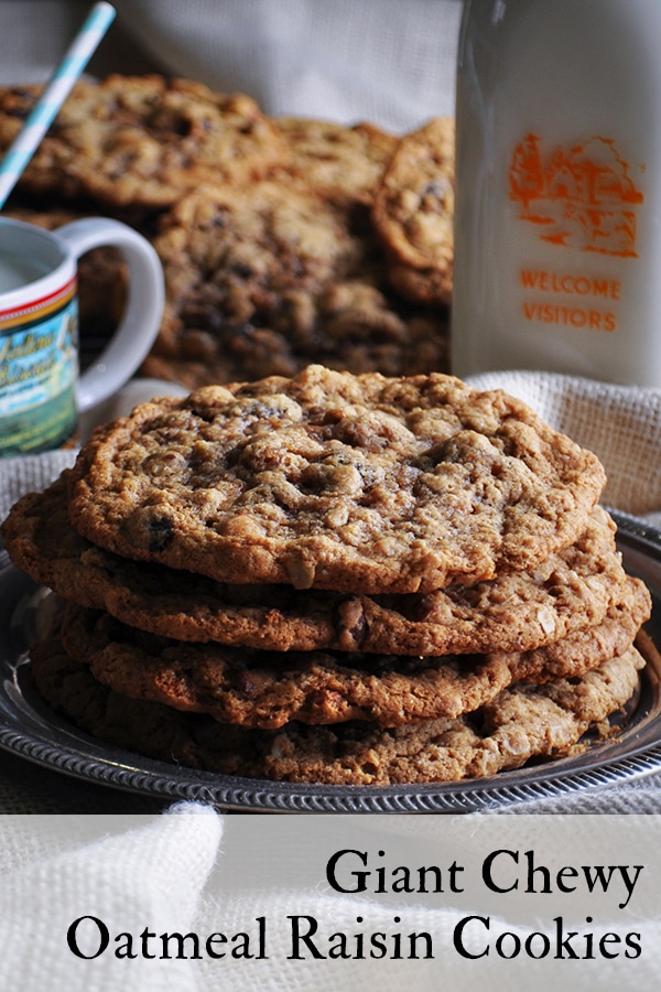 A stack of Giant Oatmeal Raisin Cookies on a plate next to a glass of milk.