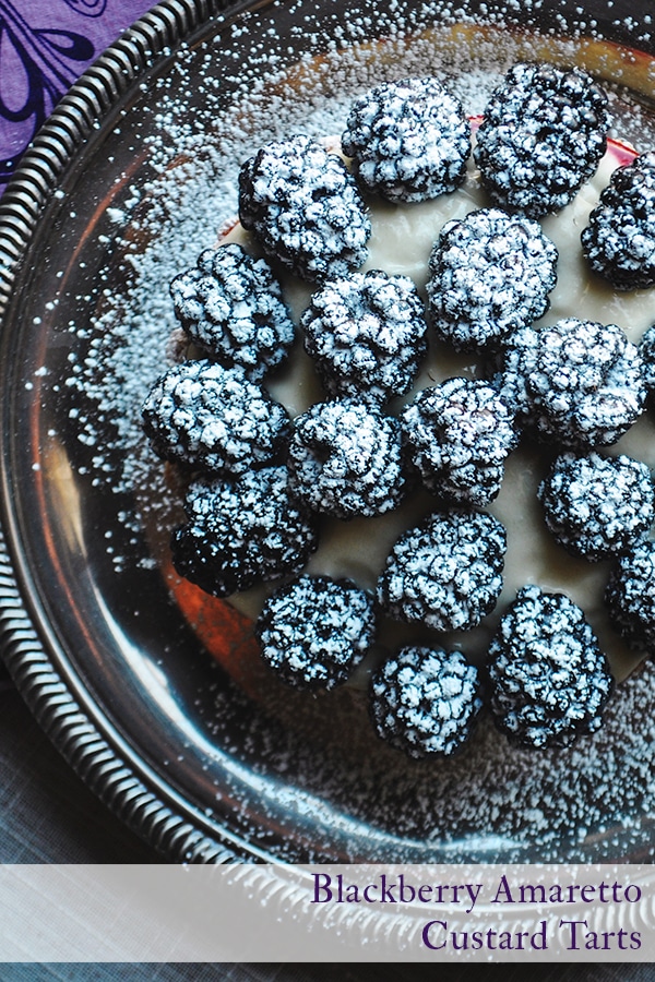 A close-up picture of a blackberry custard fruit tart sprinkled with powdered sugar.