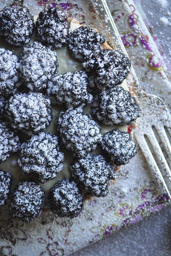 A close-up picture of a blackberry custard fruit tart sprinkled with powdered sugar.