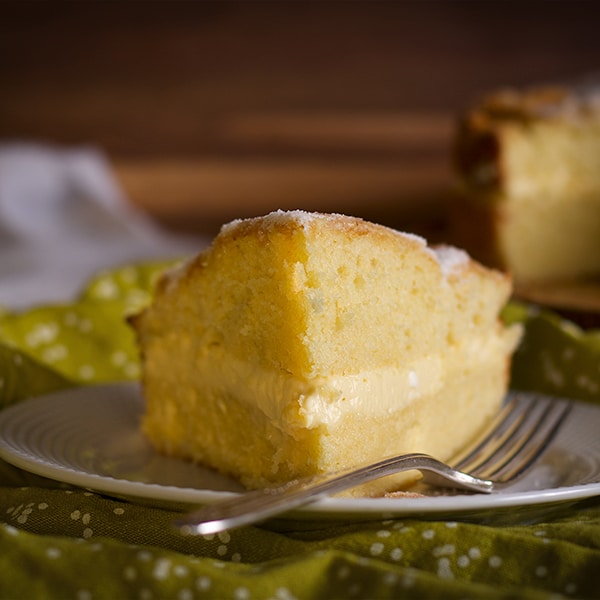 A slice of Olive Oil Cake filled with Lemon Mascarpone Pastry Cream on a plate with a fork.