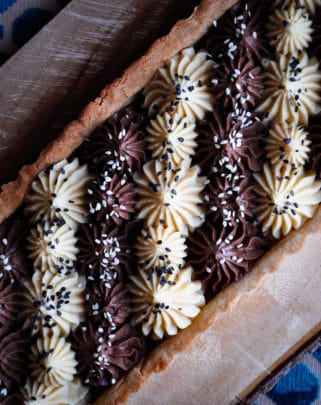 A black and white chocolate tahini tart with alternating stripes of white and dark chocolate filling.
