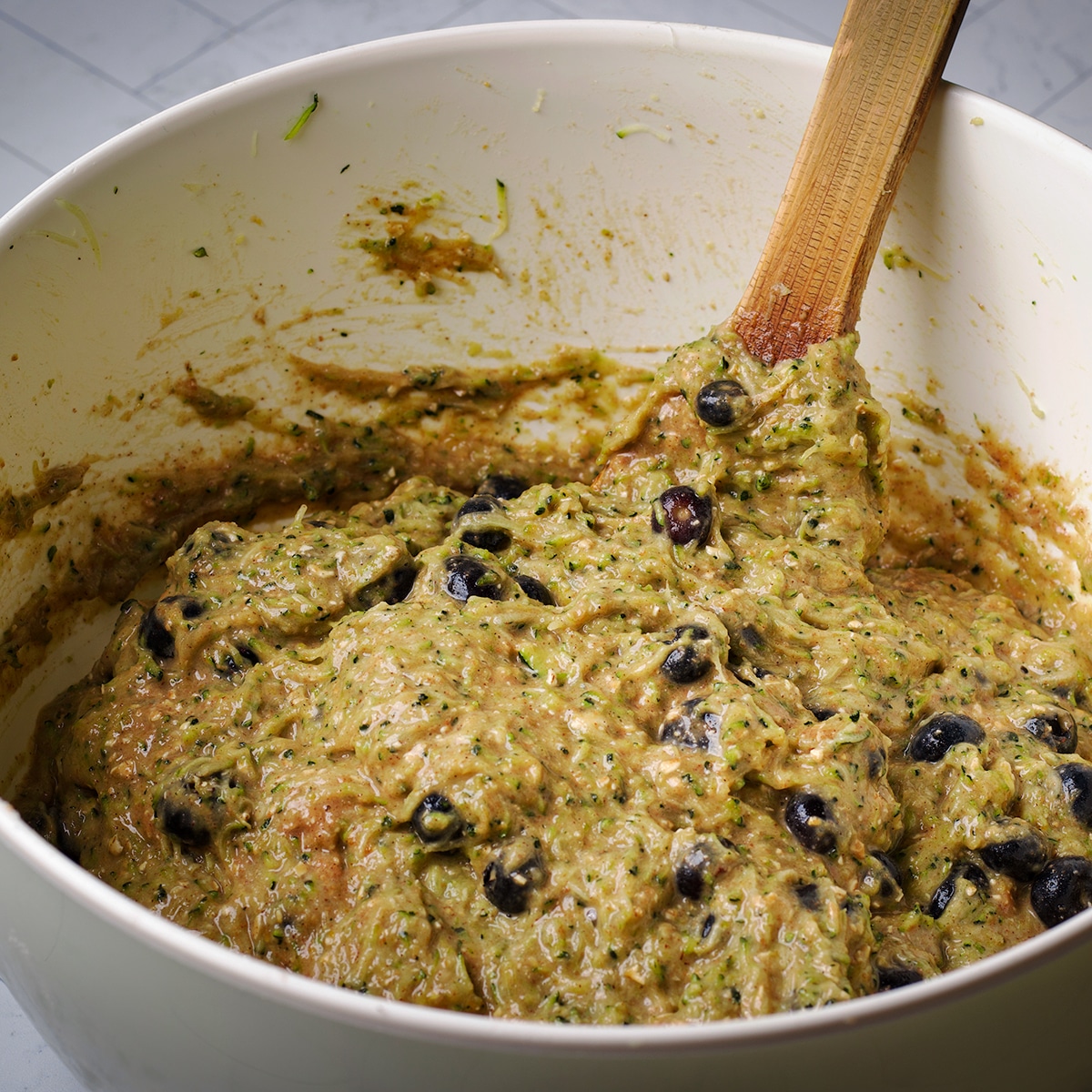 Using a wooden spoon to mix blueberries into zucchini muffin batter.