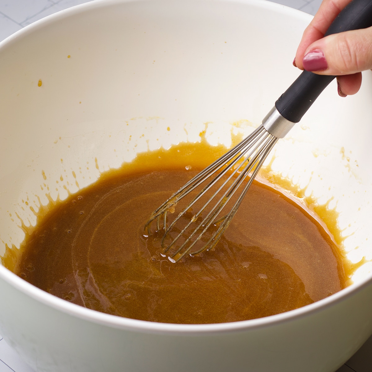 Using a wire whisk to mix brown sugar, honey, vegetable oil, eggs, vanilla, and almond extract.