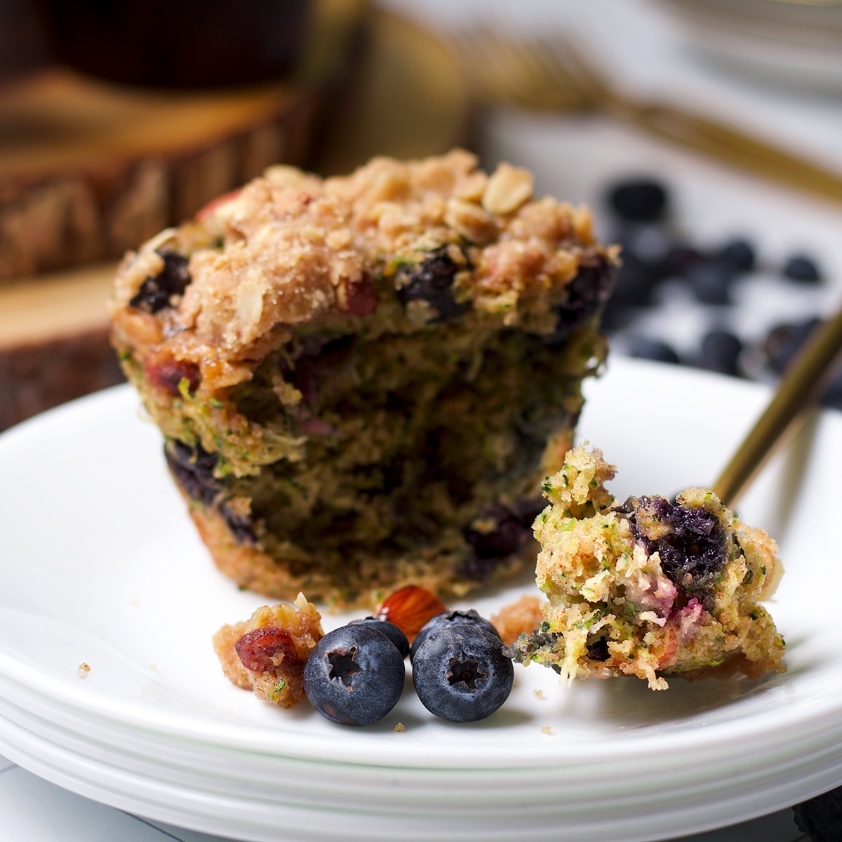 Someone using a fork to cut a bite of zucchini blueberry muffin from a muffin on a white plate.