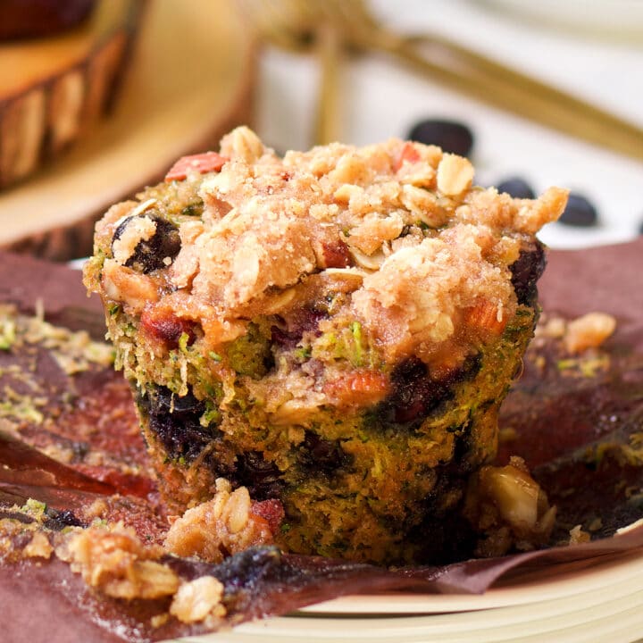 A zucchini blueberry muffin topped with streusel on a white plate.