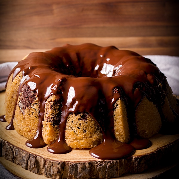 A marble cake covered in chocolate glaze on a wood tray.
