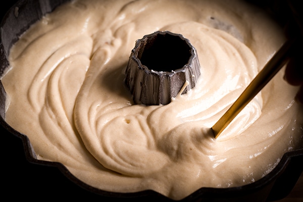 Using a knife to swirl white and dark chocolate cake batter in a bundt pan to make marble cake.